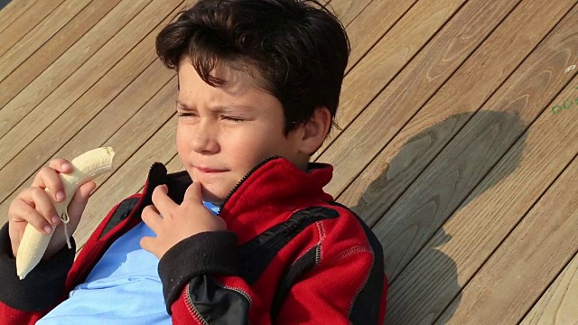 一个英俊的小男孩在户外吃香蕉的肖像视频下载