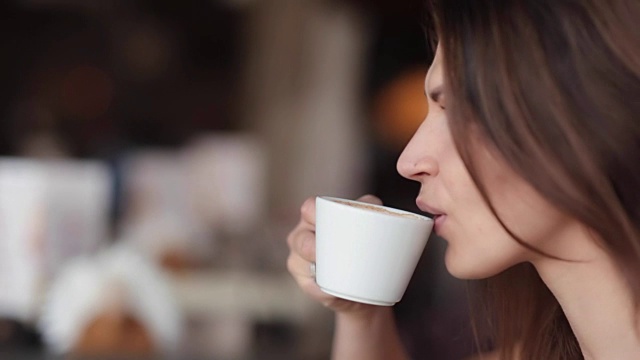 漂亮女人喜欢喝咖啡。一个漂亮女孩正喝着一杯好卡布奇诺或拿铁的侧视图，侧视图视频素材