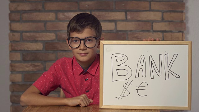 孩子坐在写字台前，手里拿着背景红砖墙上刻有字的挂图视频下载