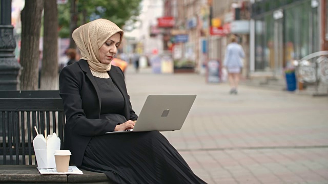 一位中东妇女在街道长凳上用笔记本电脑打字视频下载