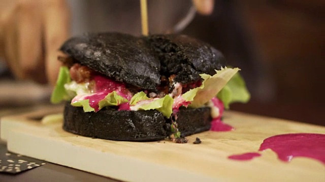 黑炭汉堡加红酱正在切。新趋势健康的黑色食品视频素材