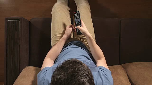 顶视图:年轻的成年男子紧张地在家里换电视频道视频下载