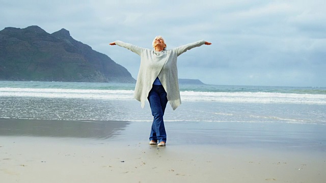 老妇人高举双手站在沙滩上视频素材