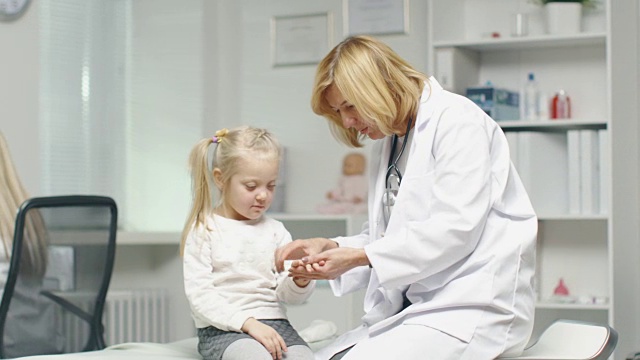 女医生正在检查一个小女孩的手。护士在后台工作。视频素材