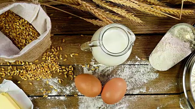 小麦，面粉，牛奶，鸡蛋和黄油放在一张木桌上，手推车，俯视图视频素材