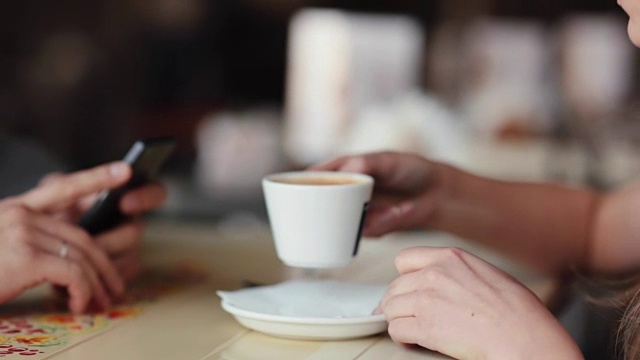 年轻女子喝咖啡的侧面图。女人喝了一杯咖啡。一个用智能手机的男人的手视频素材