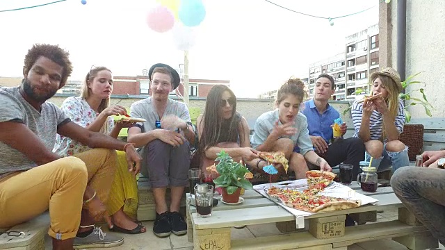 年轻人围坐在桌子旁，在屋顶露台上吃着披萨视频素材