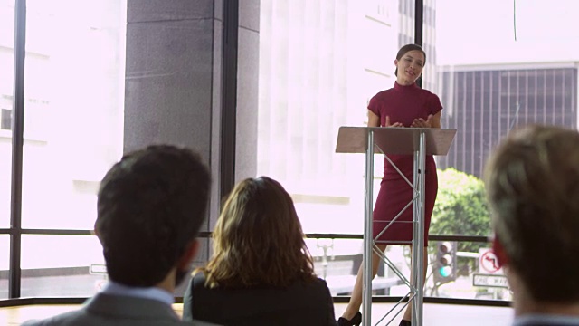 一名年轻女子在讲台上展示一场商业研讨会，由R3D拍摄视频素材