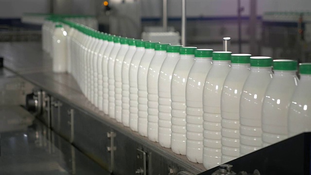 瓶子里的牛奶在传送带上移动。牛奶工厂的传送带上有绿色盖子的牛奶视频素材