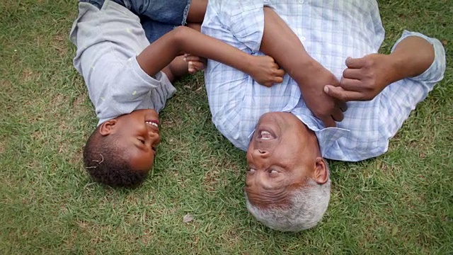 黑爷爷和小孙子躺在草地上玩，鸟瞰视频素材