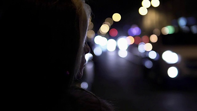 年轻的黑发女人晚上站在街上。背景是城市交通视频素材