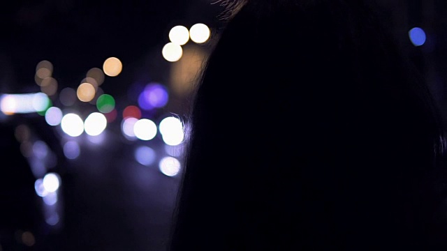 年轻的黑发女人晚上站在街上。背景是城市交通视频素材