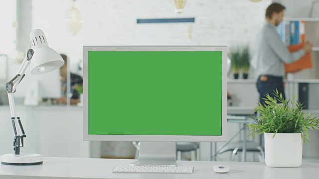 个人电脑绿色萤幕的特写。背景模糊和明亮的办公室，人们通过办公室例行公事。视频素材