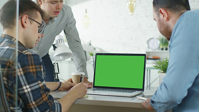 三位创意人士围绕绿屏笔记本电脑讨论业务。他们在明亮现代办公室。视频素材