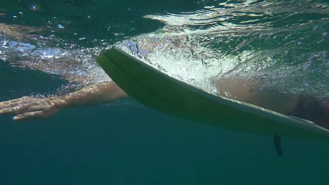 水下慢动作:一名面目全非的男性冲浪者在冲浪板上划水视频下载