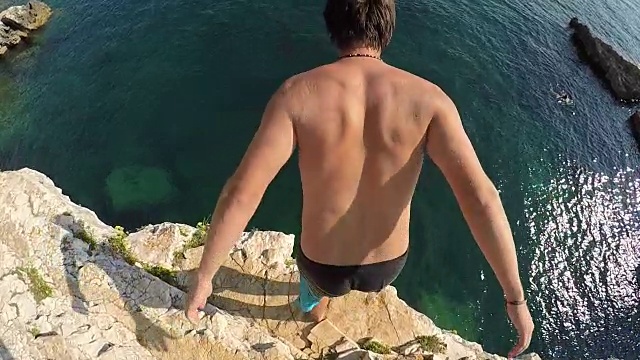 慢镜头特写:无畏的人从高高的岩石礁跳进海洋视频下载