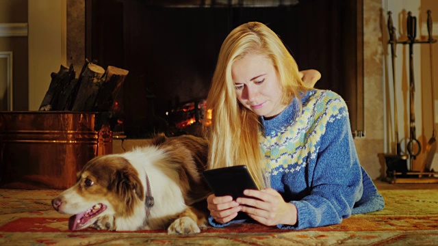 白种年轻女子躺在壁炉旁，享受着石碑。她旁边是一只狗视频素材