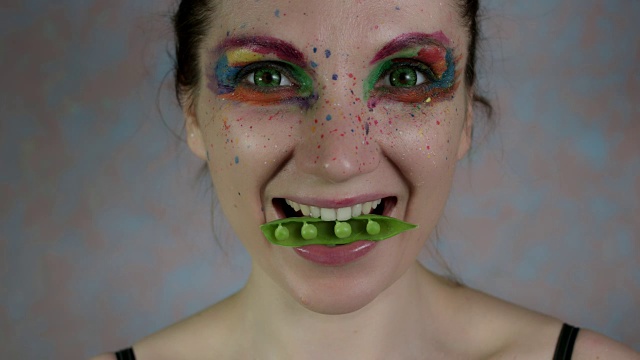 一个嘴里含着豆子的彩色化妆女人的4k照片视频下载