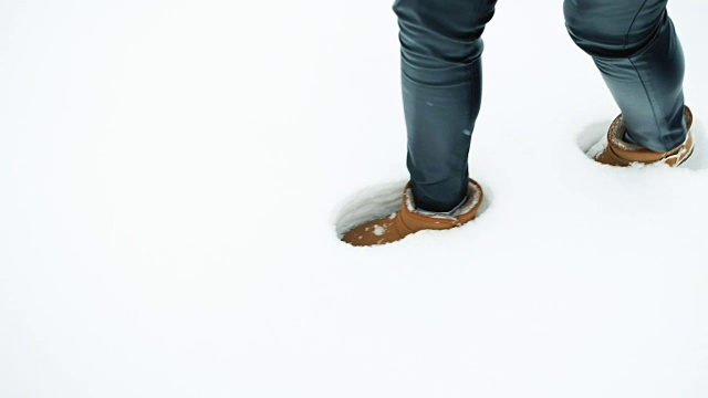 穿着棕色雪地靴的女性腿在纯净的雪地上留下了痕迹视频下载
