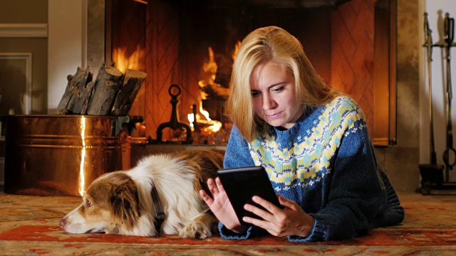和你最喜欢的狗一起休息。一个年轻的女人在壁炉的背景下看盘子上的东西视频素材