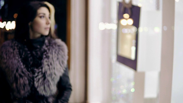 身着冬装的年轻女子走到高档精品店的橱窗前，站在橱窗前。视频下载