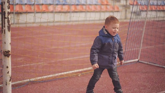 红头发的小男孩在体育场的一个足球门柱附近玩球视频素材