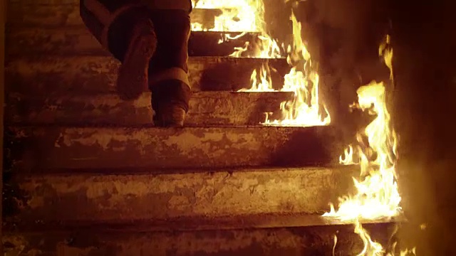 特写消防队员的腿跑上燃烧的楼梯。大楼着火了，到处可见明火。缓慢的运动。视频素材