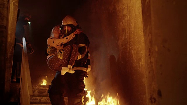 燃烧的大楼。一组消防员从燃烧的楼梯上下来。一名消防员将获救的女孩抱在怀里。视频素材