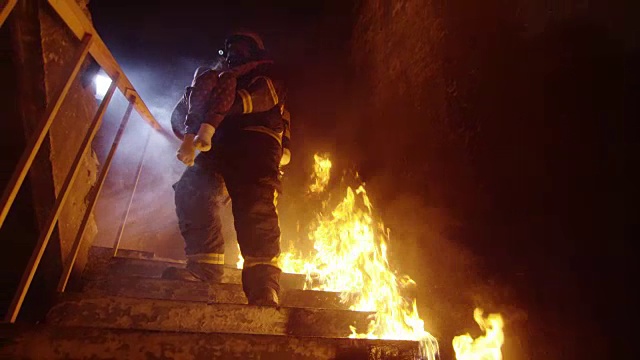 勇敢的消防员带着救下的小女孩下了燃烧的楼梯。明火随处可见。视频素材