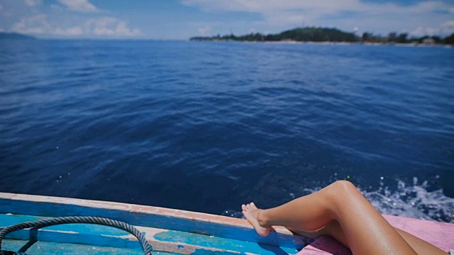 性感的腿的形象，一个年轻女子在海上巡航躺在甲板上的帆船在开放的海洋。晒黑了的女游客光着脚在游艇上穿过，背景是海洋和岛屿视频素材
