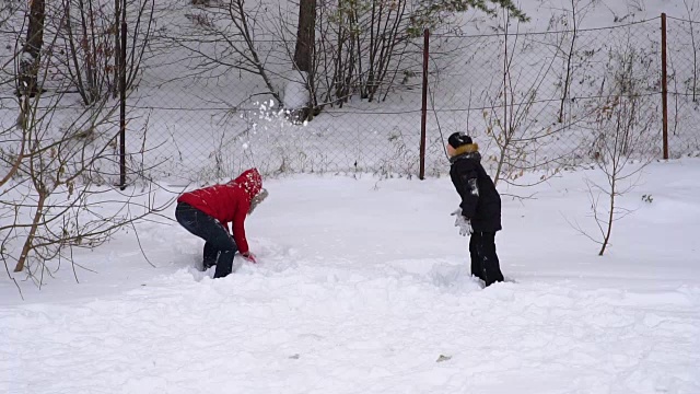 母亲和儿子吐出柔软的，新鲜的雪。一个女人和一个十几岁的男孩正在庆祝冬天。公园里一个多云的冬日。缓慢的运动。视频下载