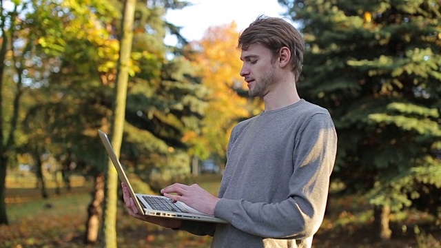 一名男子在秋季公园使用打字笔记本电脑视频下载