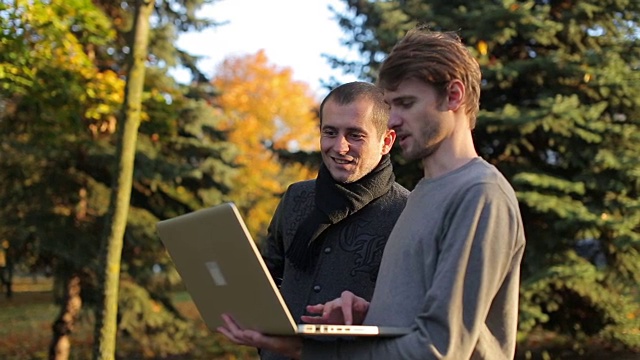 两名微笑的创业企业家在秋天的公园户外讨论分享笔记本电脑视频下载