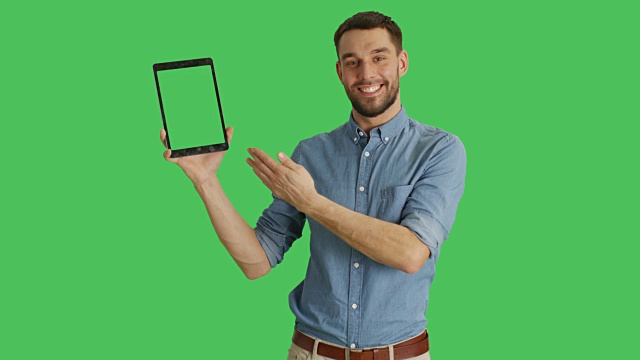 中景一个时尚的男人用一只手拿着平板电脑，用另一只手做滑动触摸手势。平板电脑和背景都是绿屏。视频下载