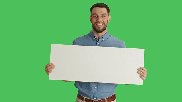 一个微笑的时尚男子拿着海报/海报的中镜头。在绿色屏幕上拍摄。视频下载