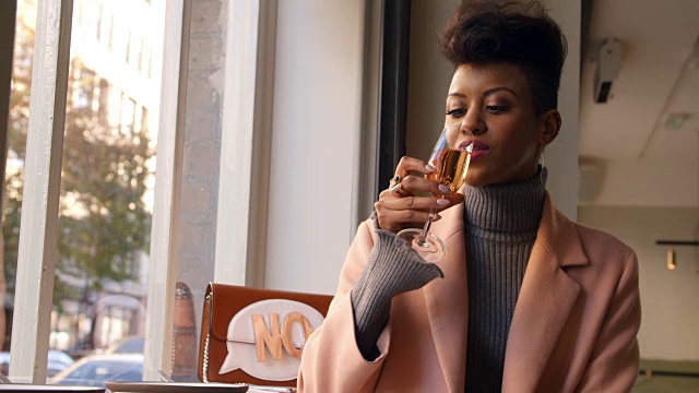 时尚的女人坐在酒吧的窗口享受饮料视频素材