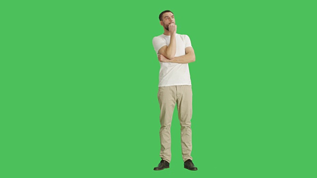 一个随意的男人环顾四周，逗乐并做触碰下巴思考手势的长镜头。拍摄在一个绿色屏幕背景。视频素材