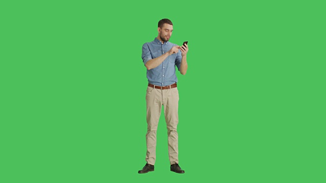 一个英俊的男人用一只手拿着智能手机，用另一只手做滑动触摸手势的长镜头。平板电脑和背景都是绿屏。视频素材