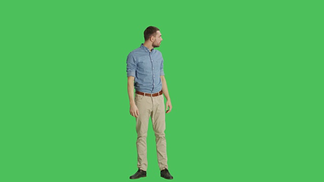 一个被逗乐的英俊男子环顾四周的长镜头。所有拍摄在一个绿色屏幕背景。视频素材