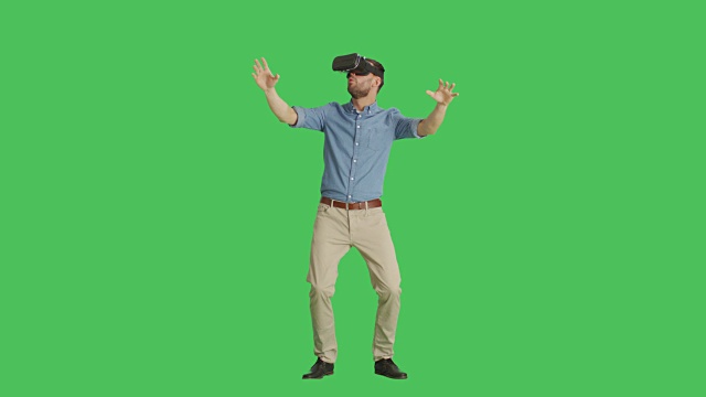 一个英俊的男人戴着虚拟现实眼镜与外部世界互动，害怕地逃跑。背景为绿幕。视频素材