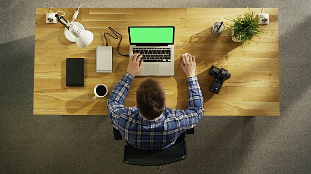 一个年轻的摄影师在他的绿屏笔记本电脑上处理照片的俯视图。相机、外置硬盘和笔记本电脑就在他身边。视频素材