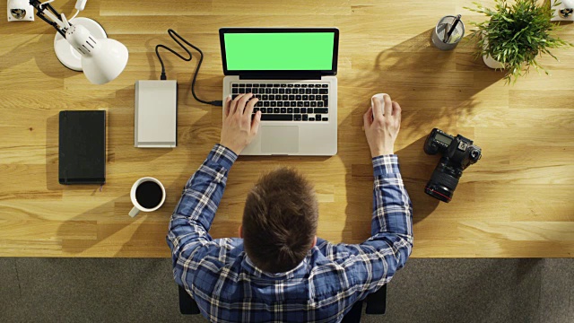 一个年轻的摄影师在他的绿屏笔记本电脑上处理照片的俯视图。相机、外置硬盘和笔记本电脑就在他身边。视频素材