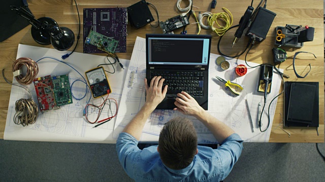 一个天才的IT技术员写代码在他的笔记本电脑坐在他的桌子上，他被各种技术组件包围。阳光照在他的桌子上。视频素材