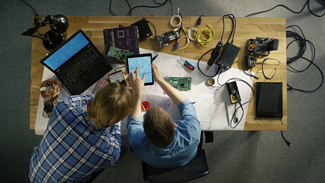 两个专业的IT技术人员讨论蓝图显示在平板电脑上的俯视图。工作空间充满了技术组件视频素材