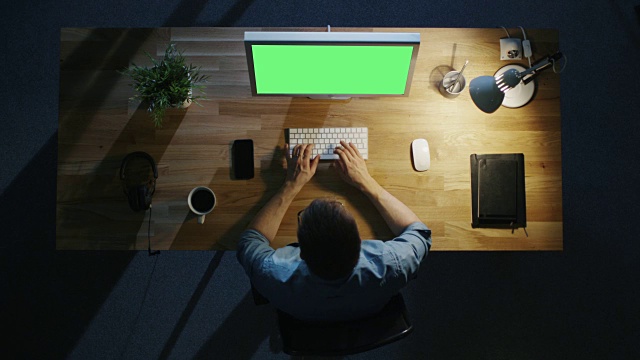 顶视图的创造性的人在他的桌面电脑与模型的绿色屏幕在晚上。台灯打开。视频素材