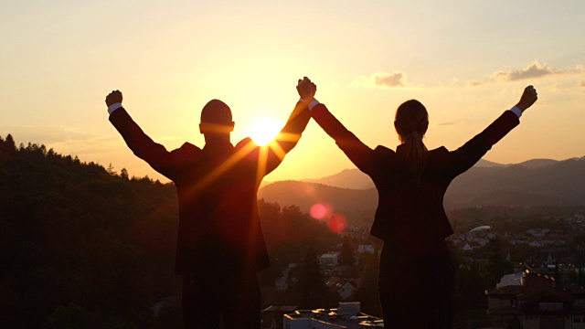 特写:日落时分，摩天大楼顶上的两名员工在空中举起双手视频下载