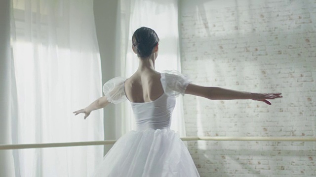 年轻美丽的芭蕾舞女演员优雅地在她的尖芭蕾舞鞋上跳舞。她穿着白色芭蕾舞裙。工作室是阳光和现代。在缓慢的运动。视频素材