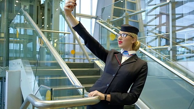 金发空姐站在楼梯上用智能手机自拍视频素材
