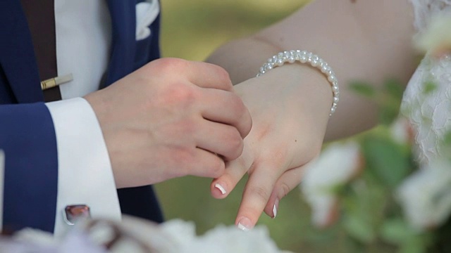 新娘和新郎在绿色的自然背景下交换结婚戒指的特写视频下载