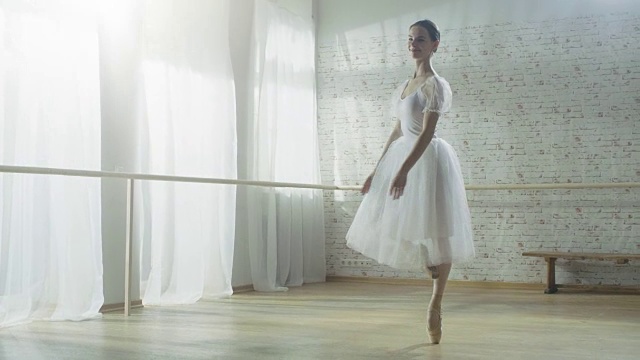 年轻美丽的芭蕾舞者在她的尖芭蕾舞鞋上热情而优雅地跳舞，她正在旋转。她穿着白色芭蕾舞裙。工作室是阳光和现代。视频素材